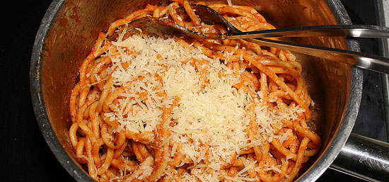 Spgahetti mit Sauce und Reibkäse in der Pfanne vermischen